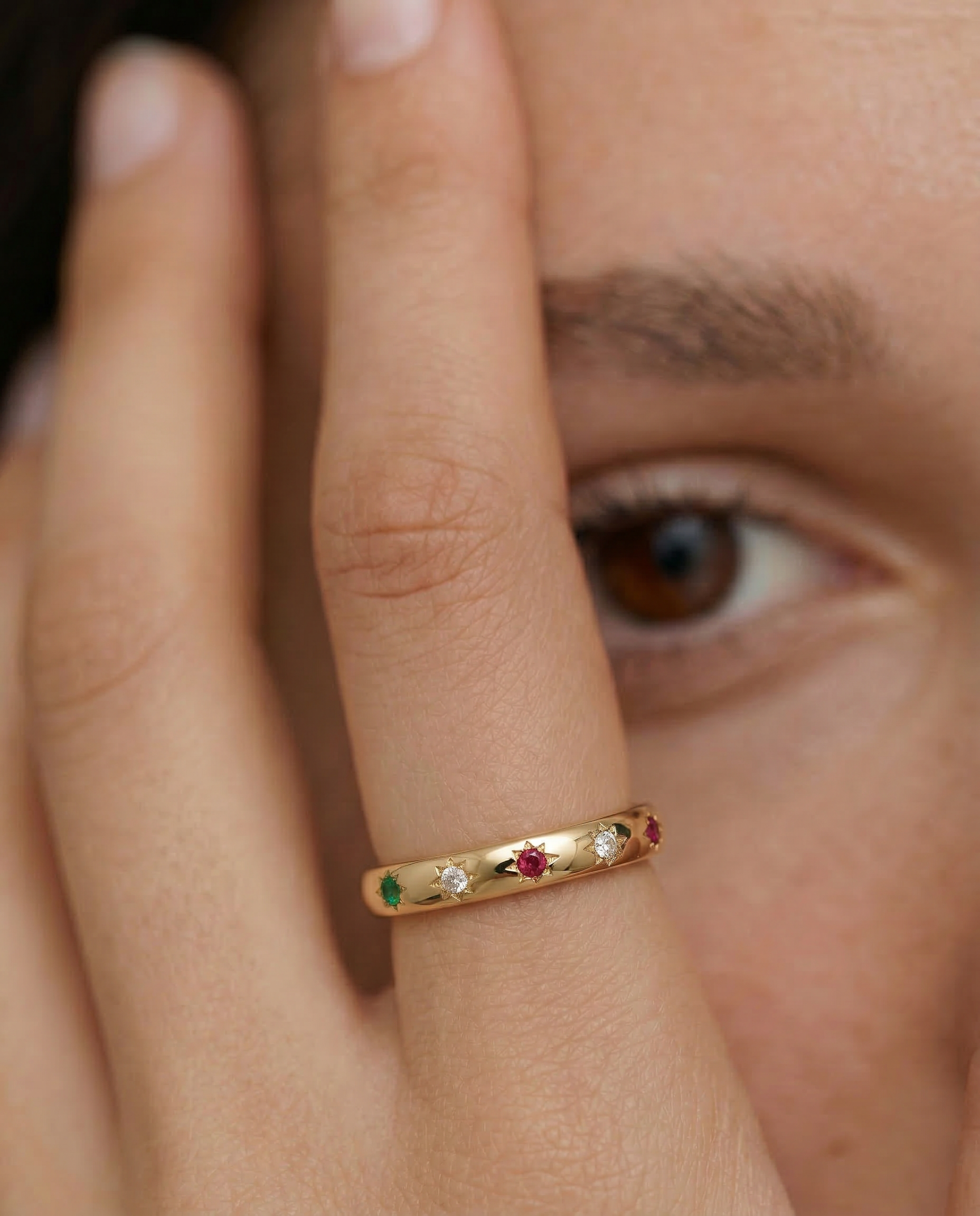 model wearing a gold-plated ring with a series of vibrant gemstones set in star-shaped bezels along the polished band