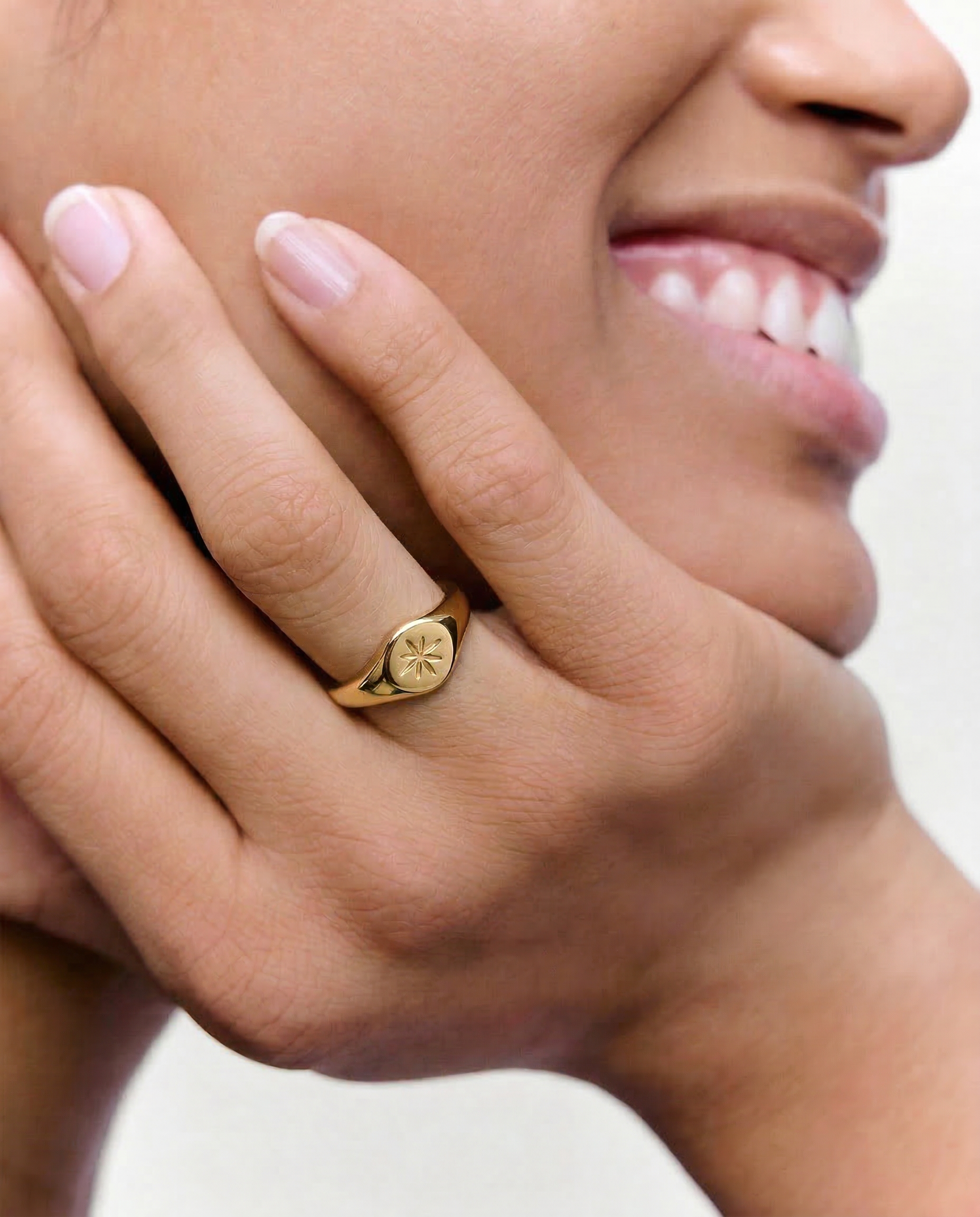 close up of a model wearing a gold signet ring with a star engraving on the top, crafted from gold-plated metal.