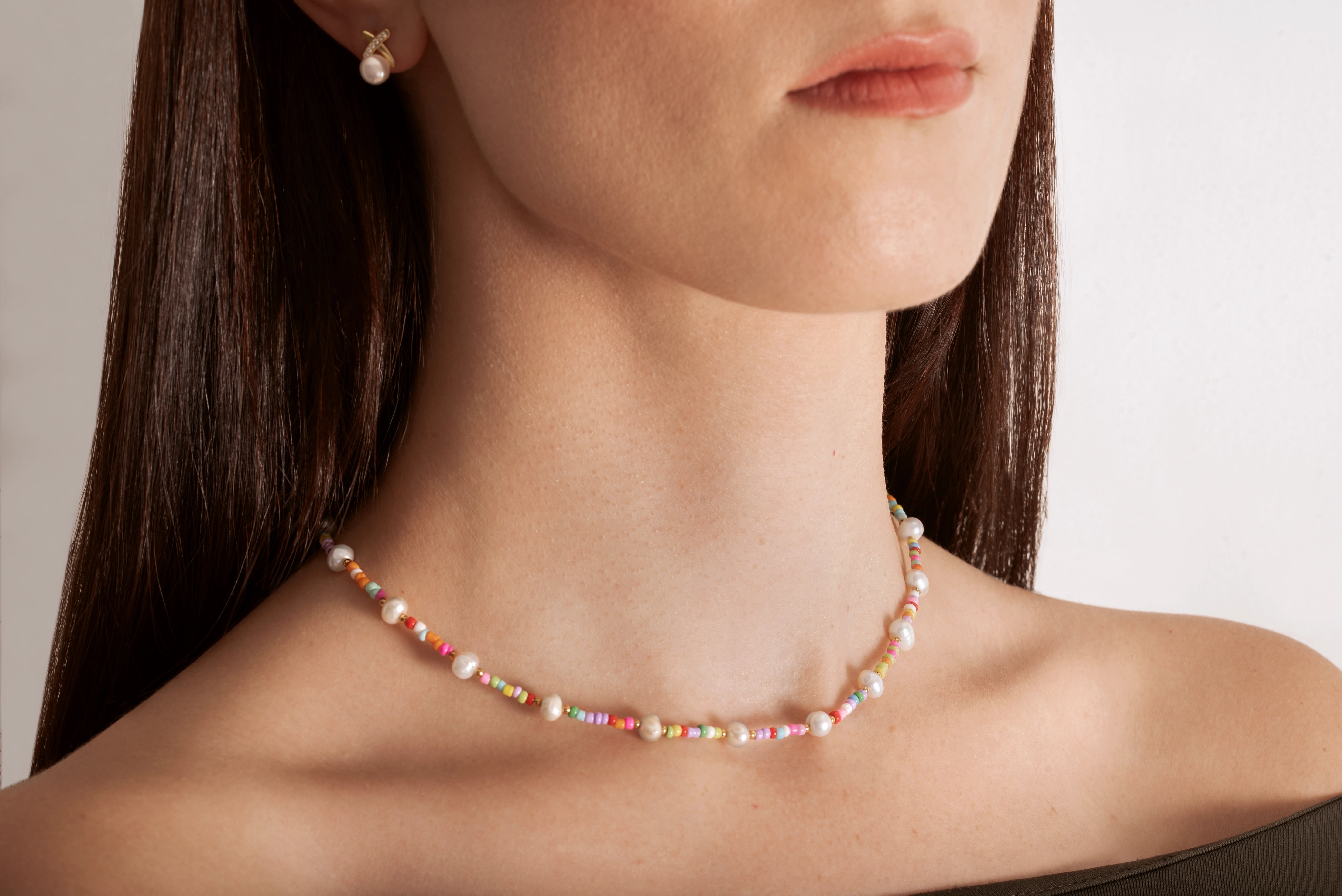 model wearing a colorful necklace with white freshwater pearls and multicolored beads, featuring a gold-colored chain and a heart charm.