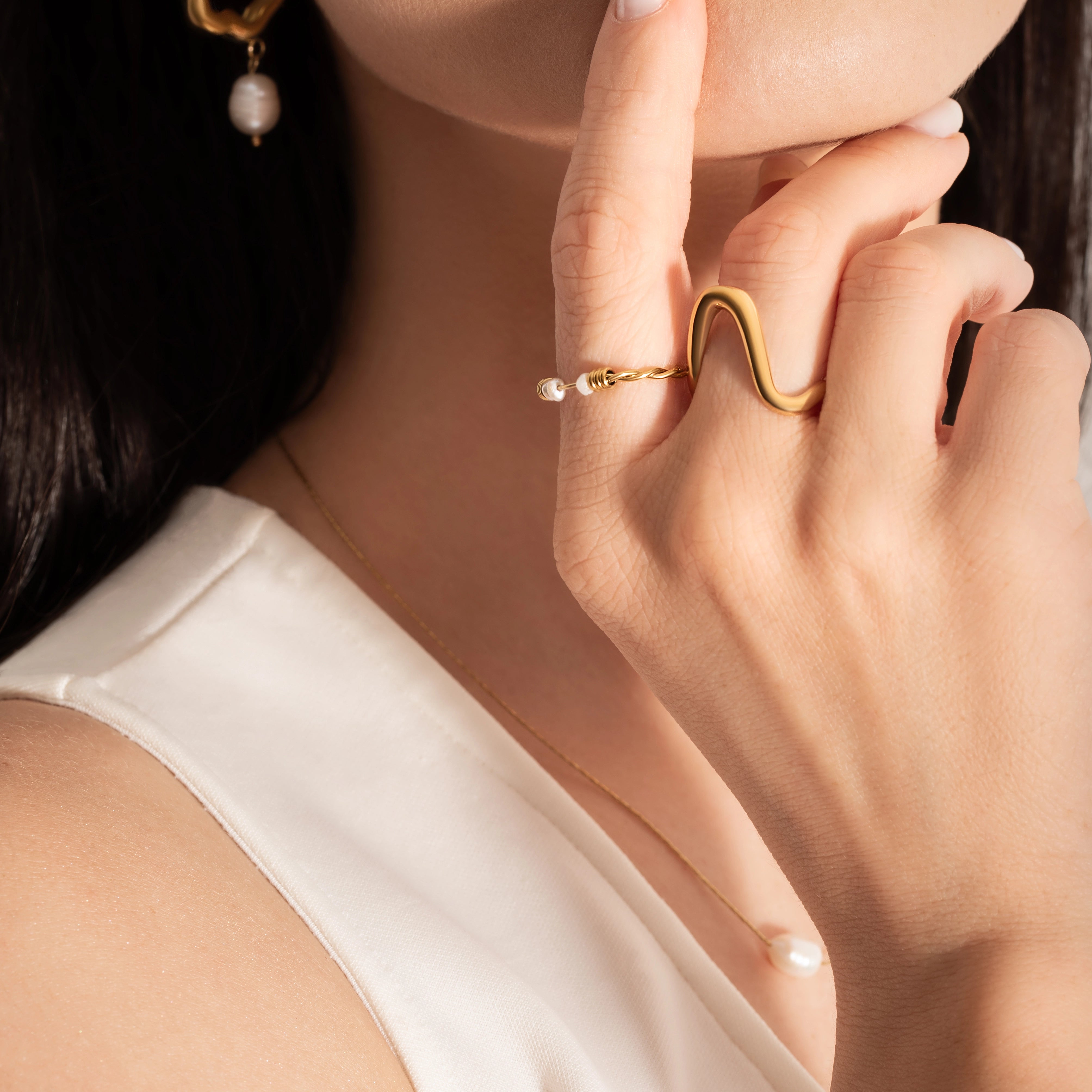 close up of a model wearing intertwined delicate gold plated ring with natural freshwater pearls