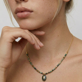 Close-up of a person wearing a gold-toned necklace with natural African turquoise beads in shades of sage, moss, and earth tones, featuring a smooth oval pendant.