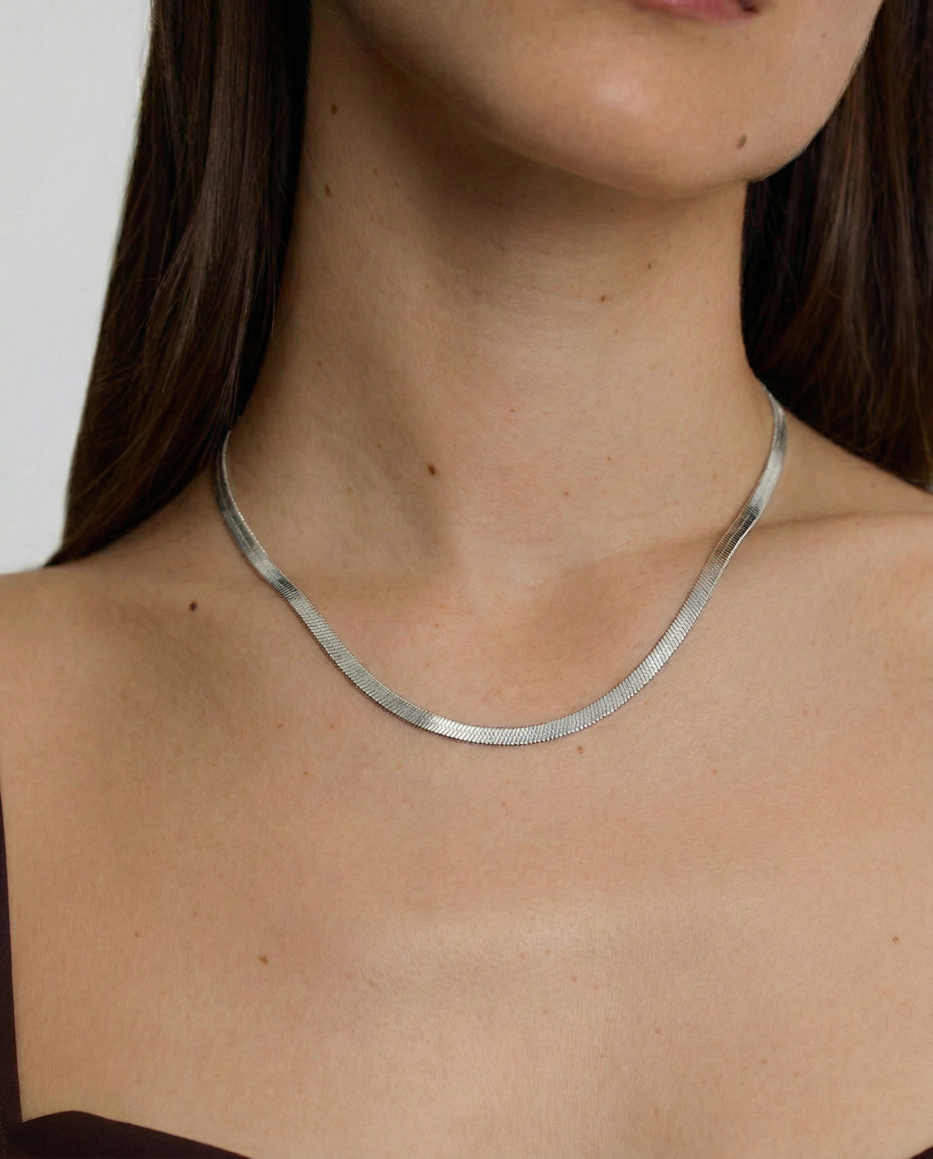 model wearing a sleek sterling silver herringbone chain necklace with an adjustable length and a heart charm