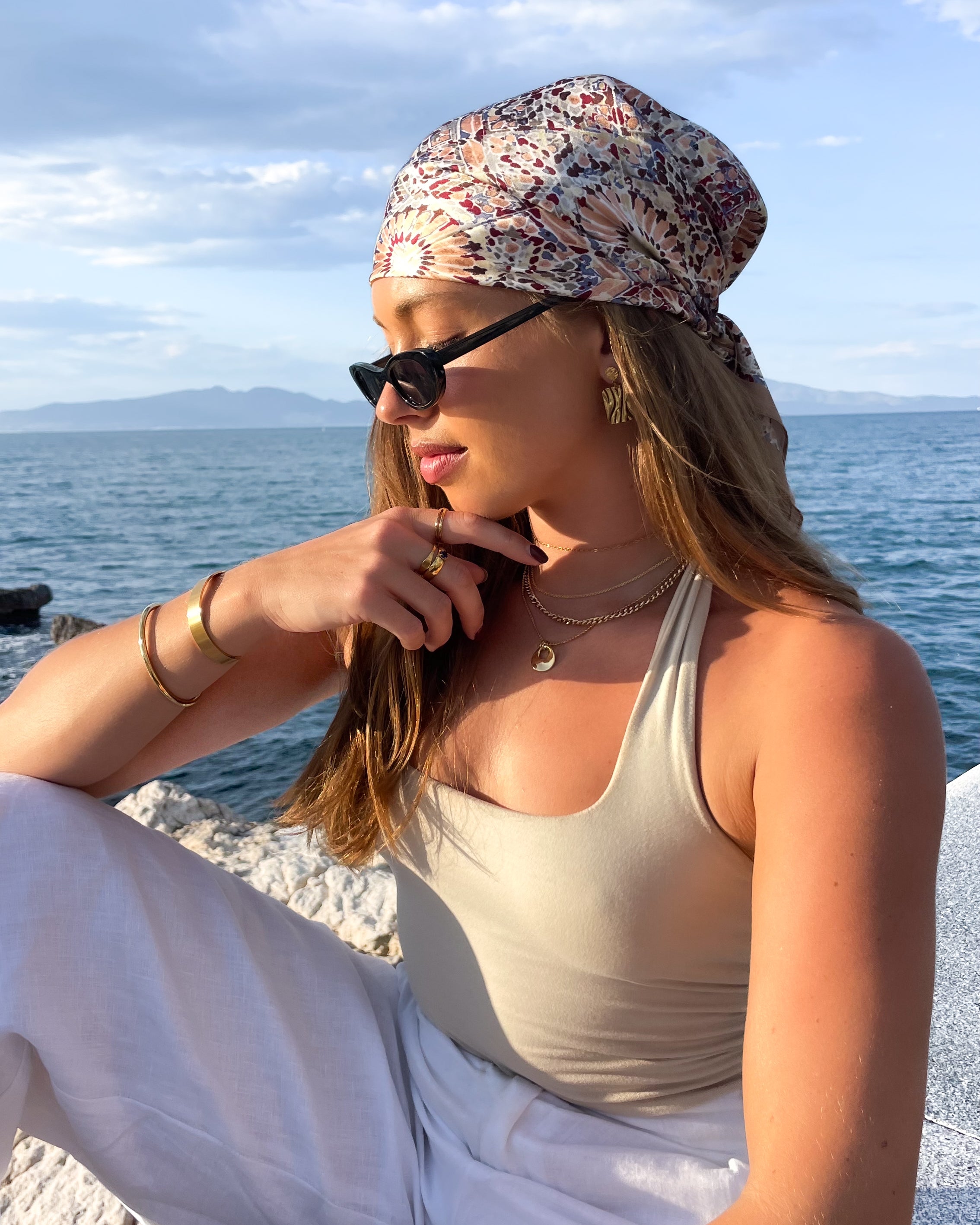 Woman sitting by the ocean wearing multiple gold plated jewellery