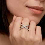 Close-up of a woman's hand wearing a silver-colored ring with an X-shaped design and sparkling cubic zirconia stones on the intersections.