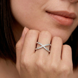 Close-up of a woman's hand wearing a silver-colored ring with an X-shaped design and sparkling cubic zirconia stones on the intersections.