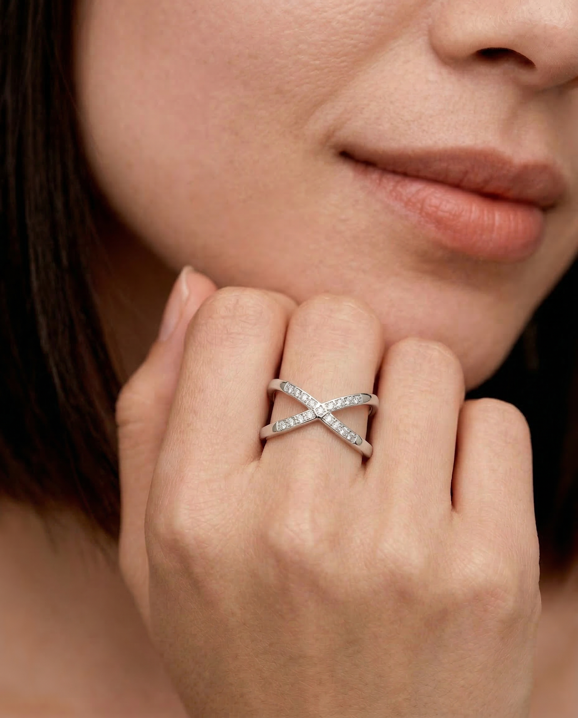 Close-up of a woman's hand wearing a silver-colored ring with an X-shaped design and sparkling cubic zirconia stones on the intersections.