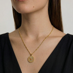 Gold necklace with a round pendant worn by a person against a neutral background
