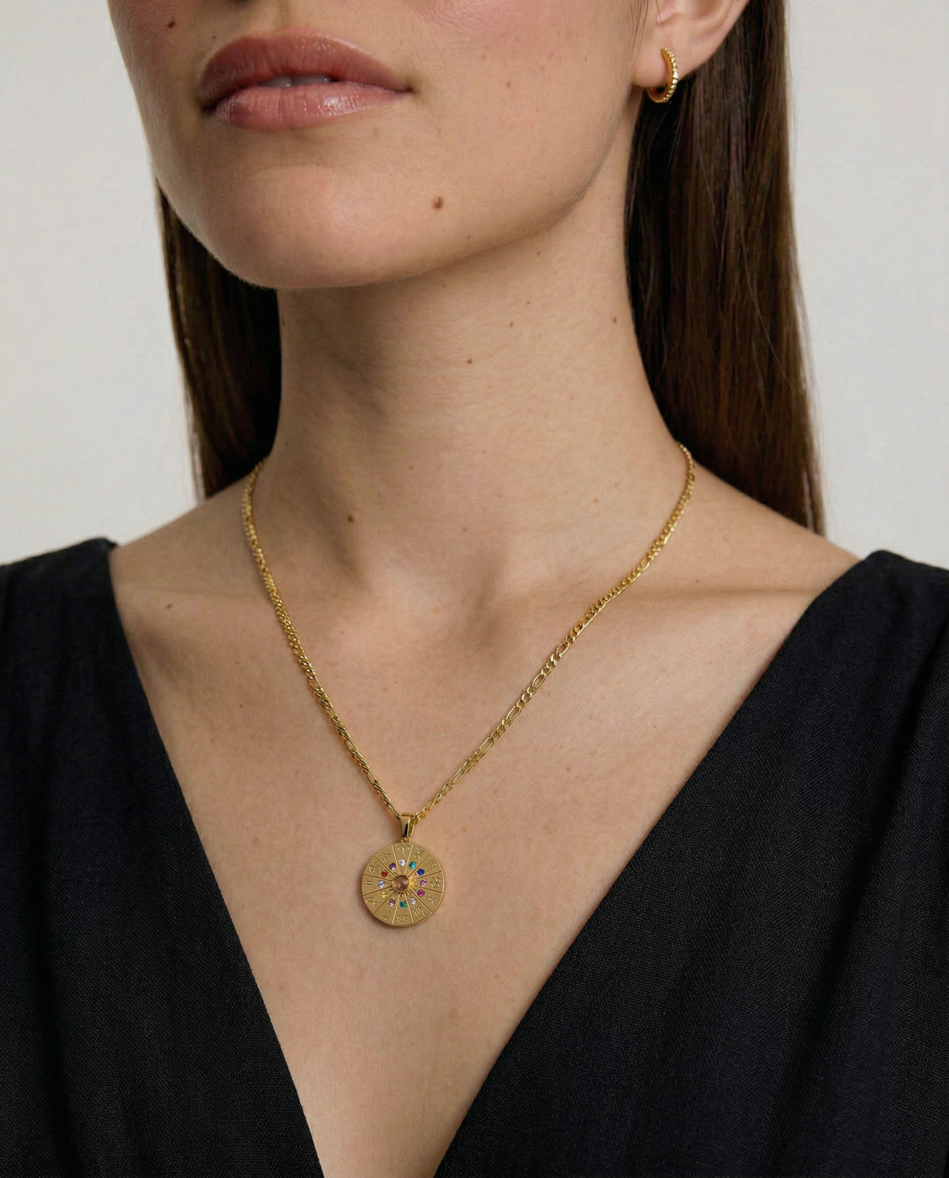 Gold necklace with a round pendant worn by a person against a neutral background