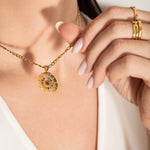 model wearing A gold-plated curb chain necklace with a round zodiac wheel pendant featuring multicolored sparkling crystals and a central moonstone.