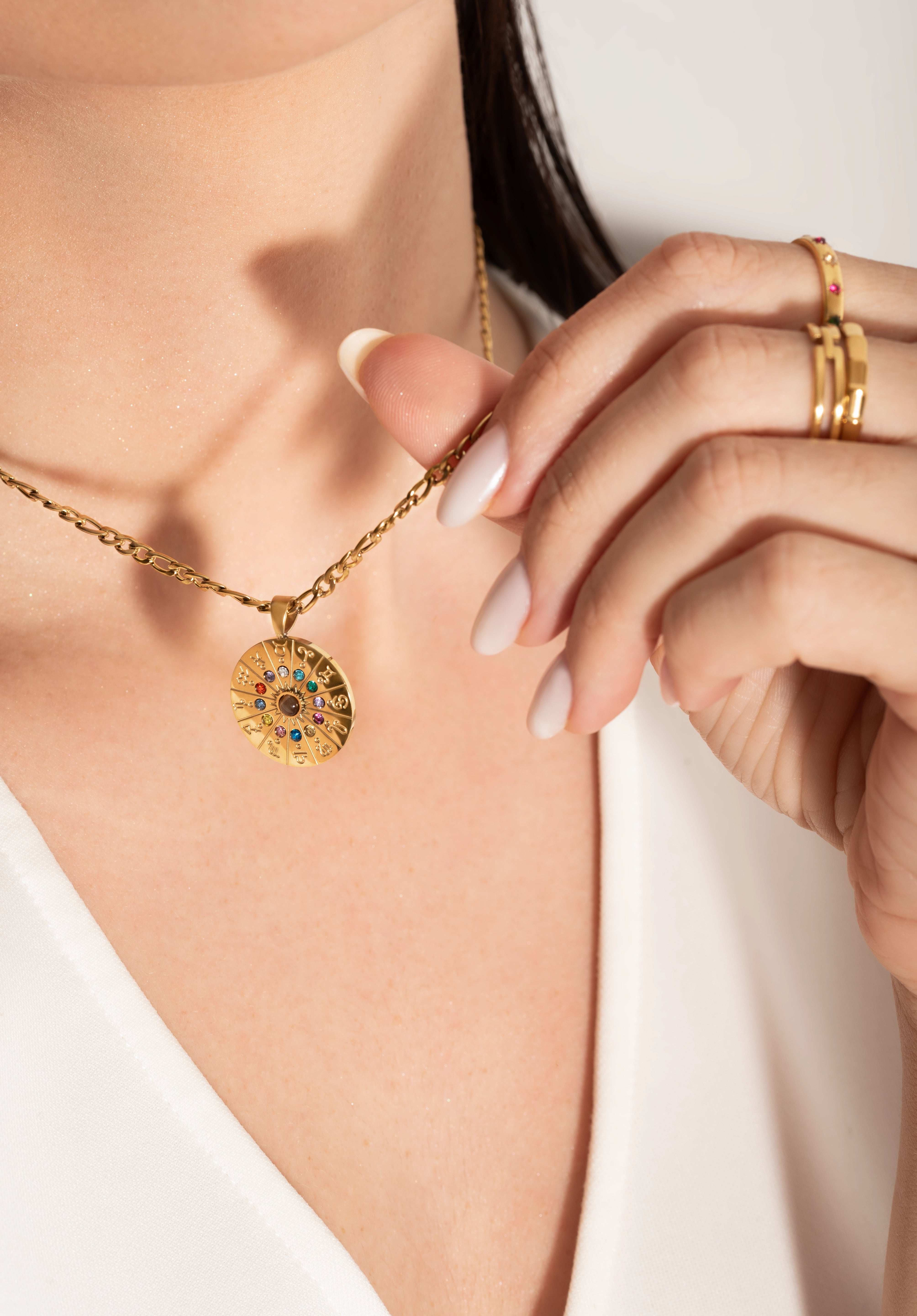 model wearing A gold-plated curb chain necklace with a round zodiac wheel pendant featuring multicolored sparkling crystals and a central moonstone.