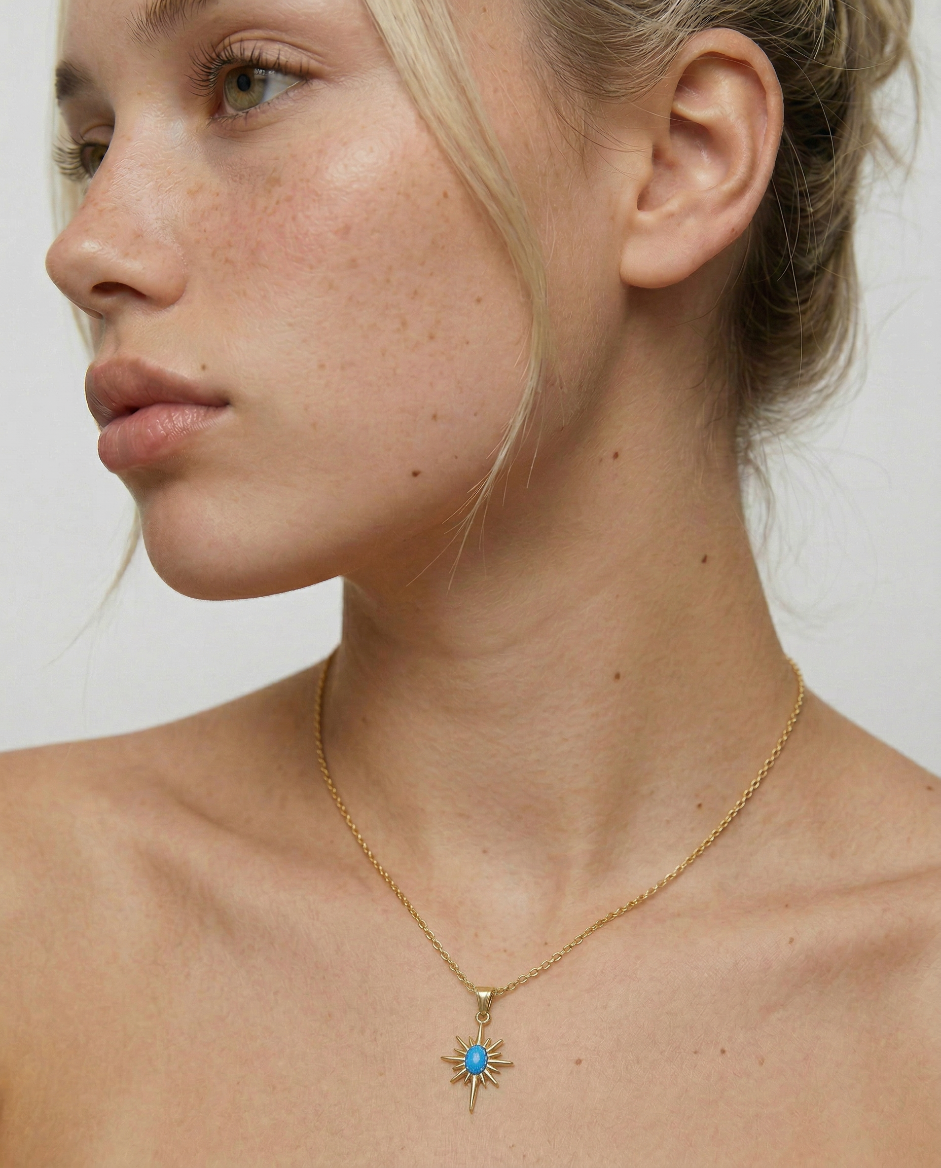 model wearing a gold-plated necklace with a starburst pendant featuring a blue opal in the center