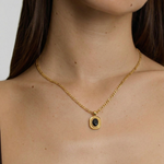 model wearing an 18k gold-plated stainless steel necklace with a polished Figaro chain and an oval medallion pendant featuring a deep black onyx stone