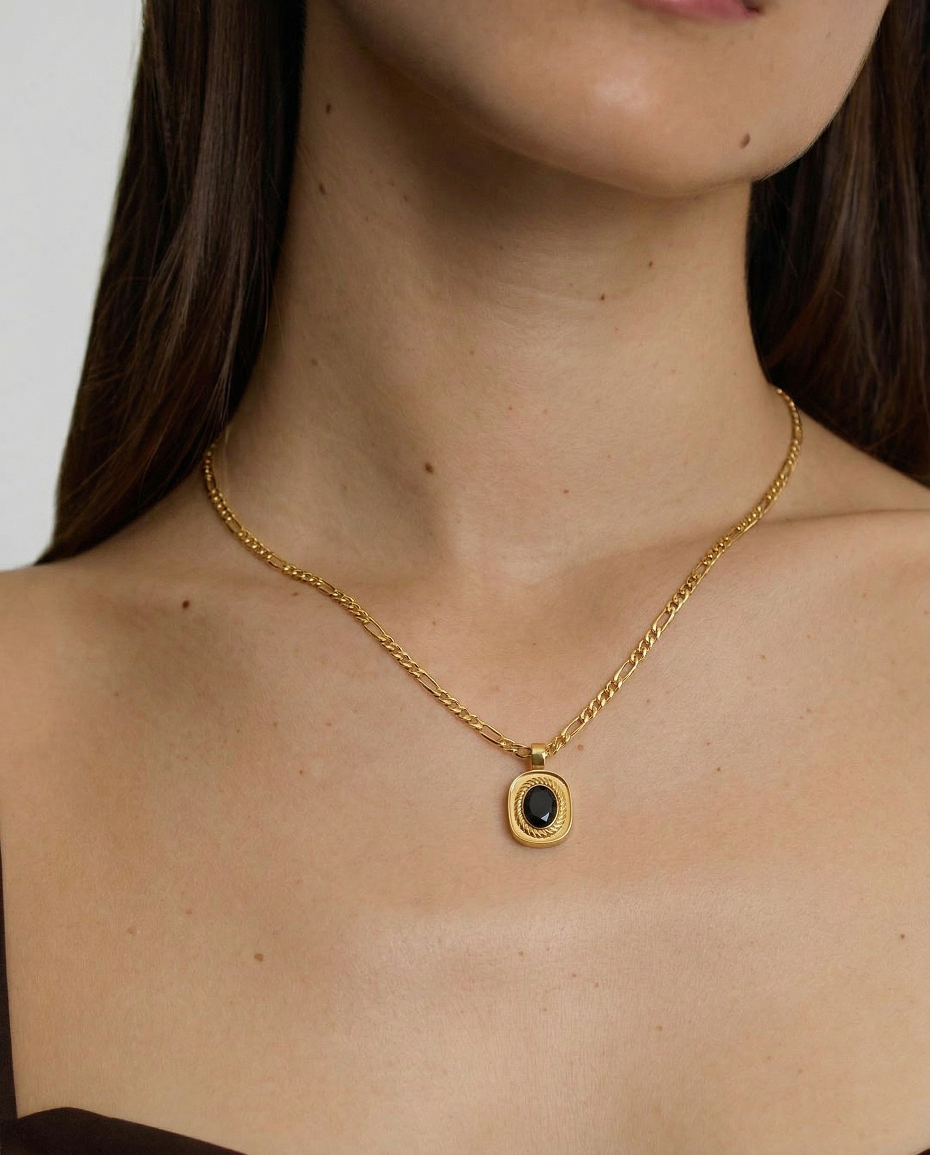 model wearing an 18k gold-plated stainless steel necklace with a polished Figaro chain and an oval medallion pendant featuring a deep black onyx stone