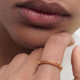 Close-up of a person wearing a gold ring on their finger with a neutral background