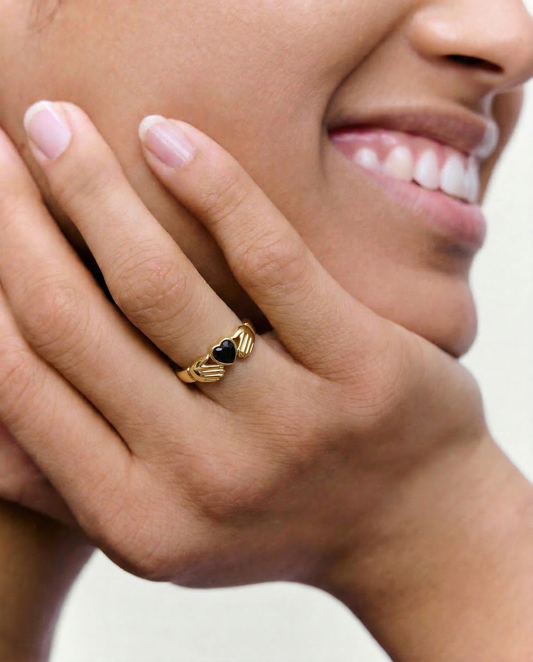 close up of a model wearing a statement gold plated ring with 2 hands holding a black heart