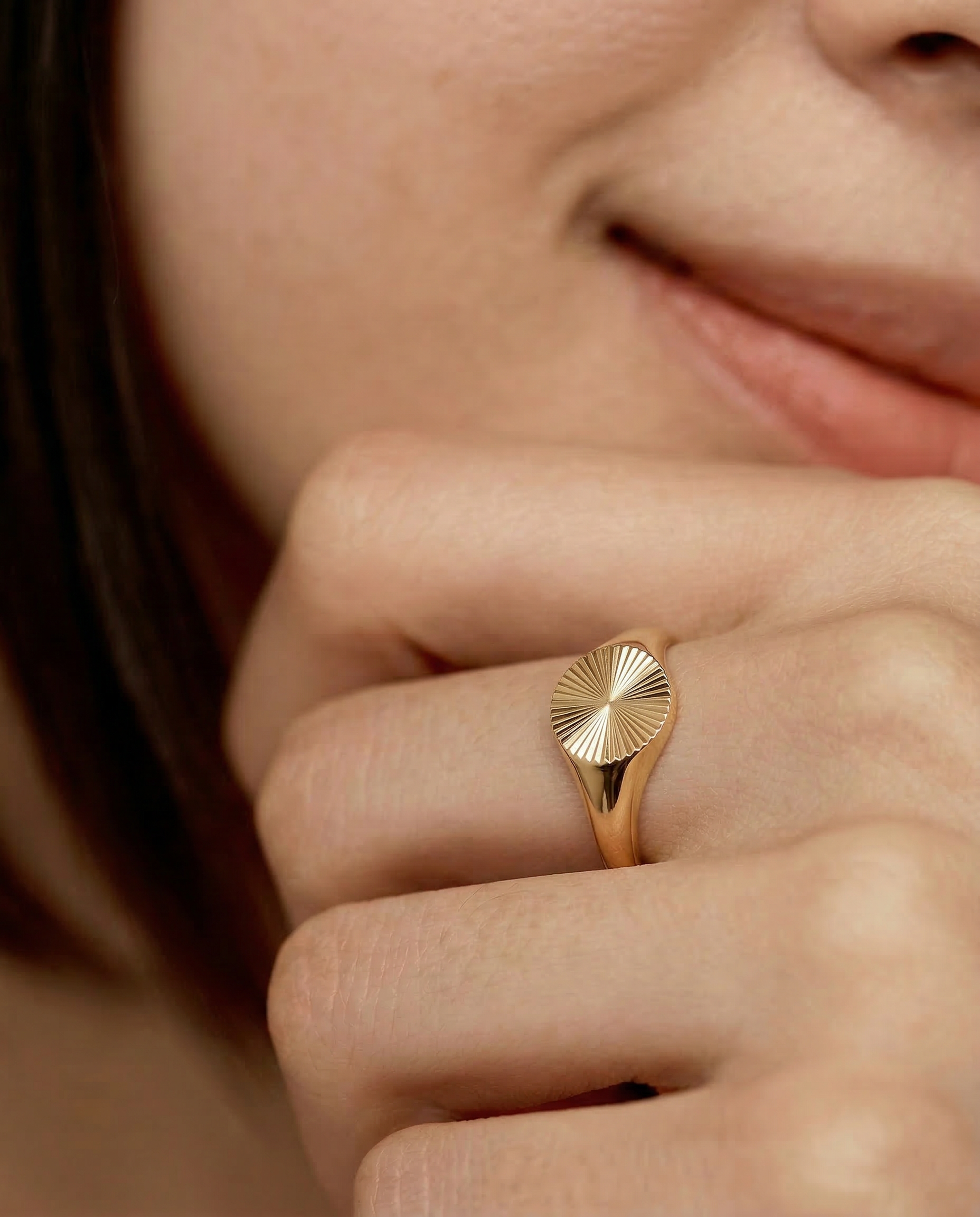 close up of a model wearing a gold-plated signet ring with an oval face featuring a sunburst pattern
