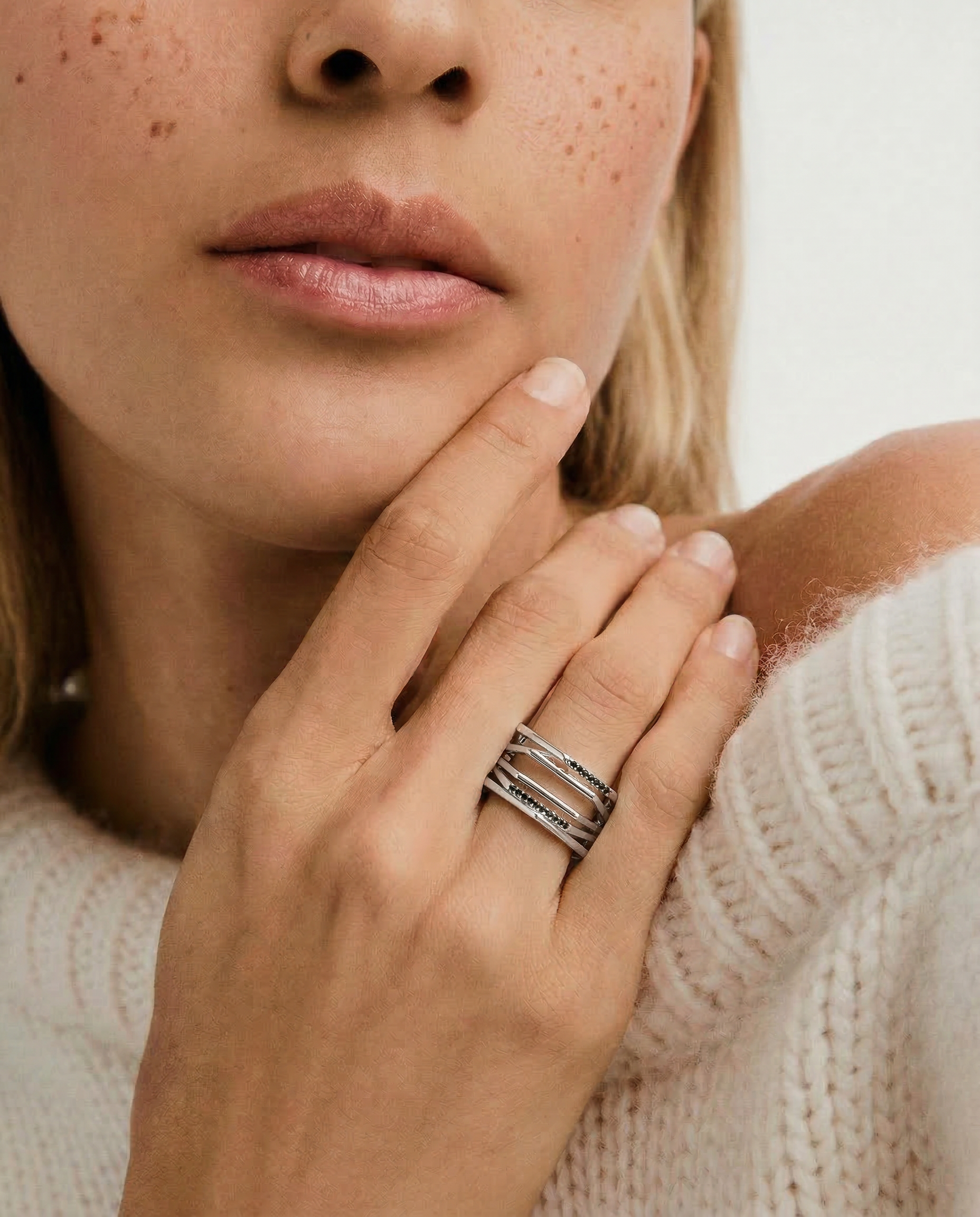 close shot of a model wearing a silver ring with a hexagonal design featuring geometric flowing lines and black crystal accents on the edges