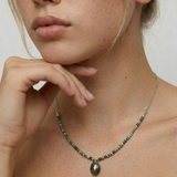 Close-up of a person wearing a necklace with variegated African turquoise beads and silver spacers, ending in a teardrop-shaped pendant