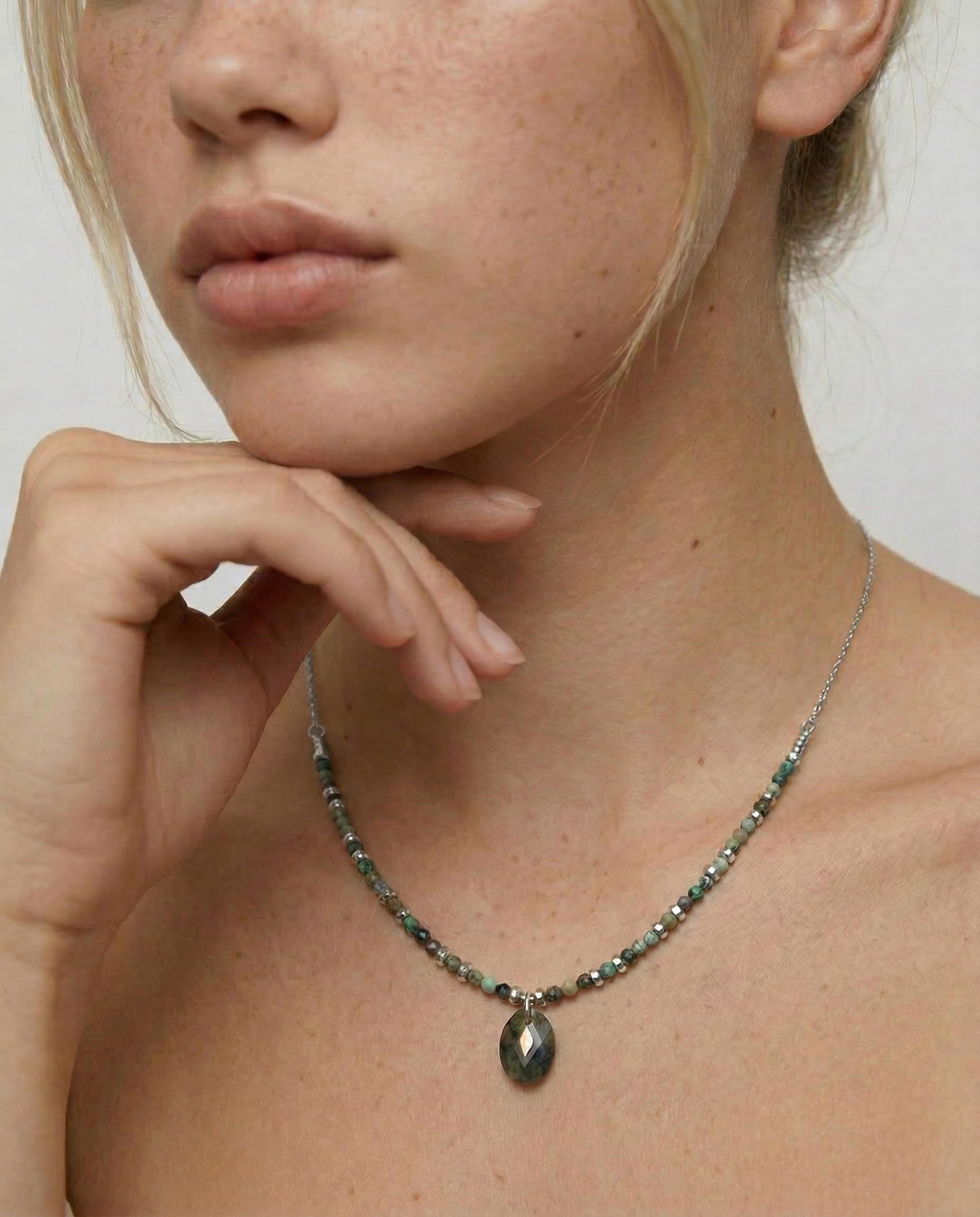 Close-up of a person wearing a necklace with variegated African turquoise beads and silver spacers, ending in a teardrop-shaped pendant