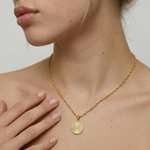 Gold necklace with a circular pendant worn by a person against a neutral background