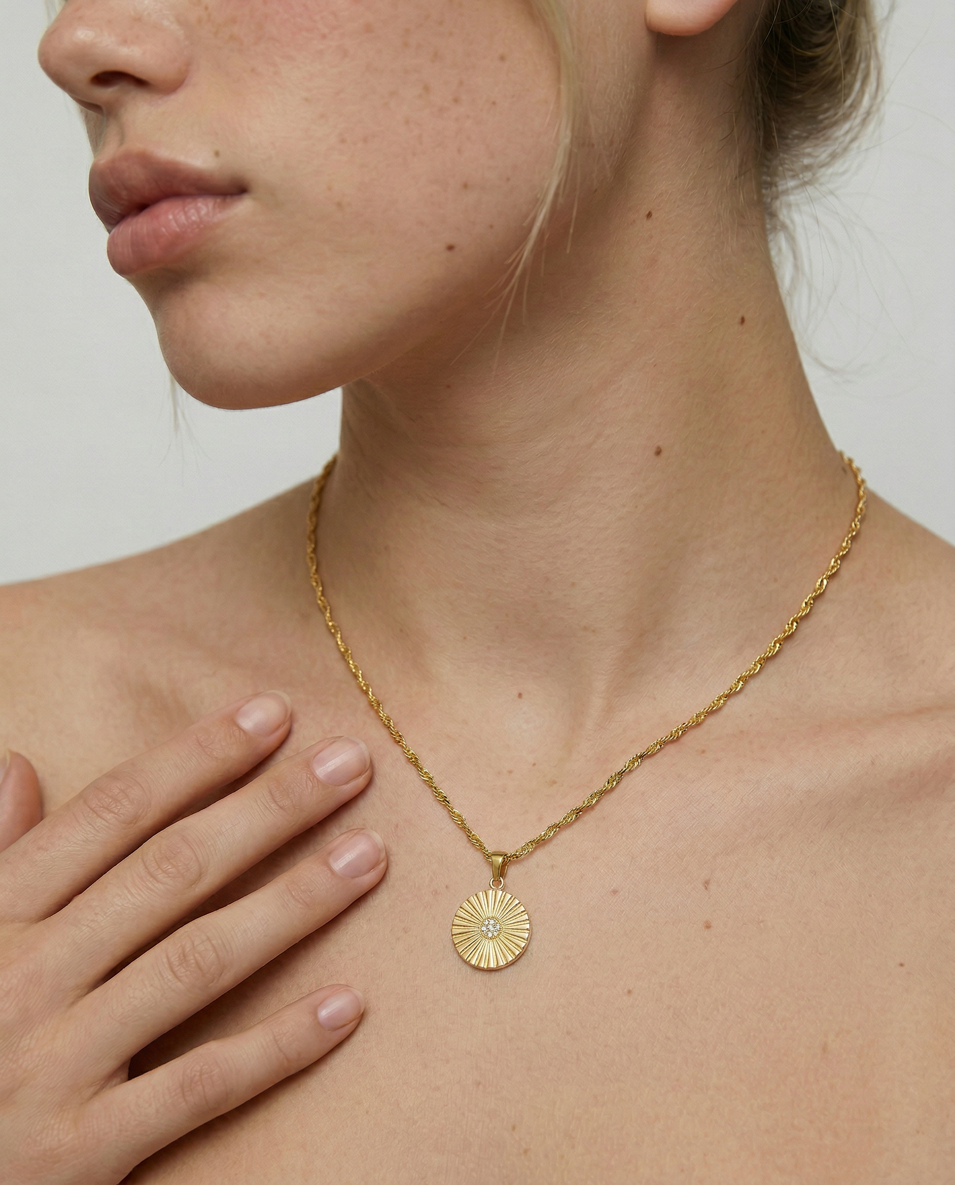 Gold necklace with a circular pendant worn by a person against a neutral background