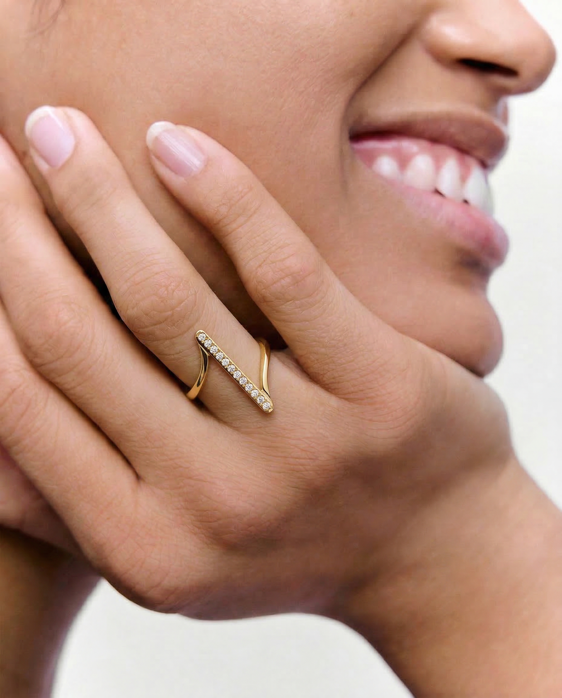 model wearing a contemporary gold-plated ring with an asymmetric design featuring a sleek bar adorned with a line of sparkling stones
