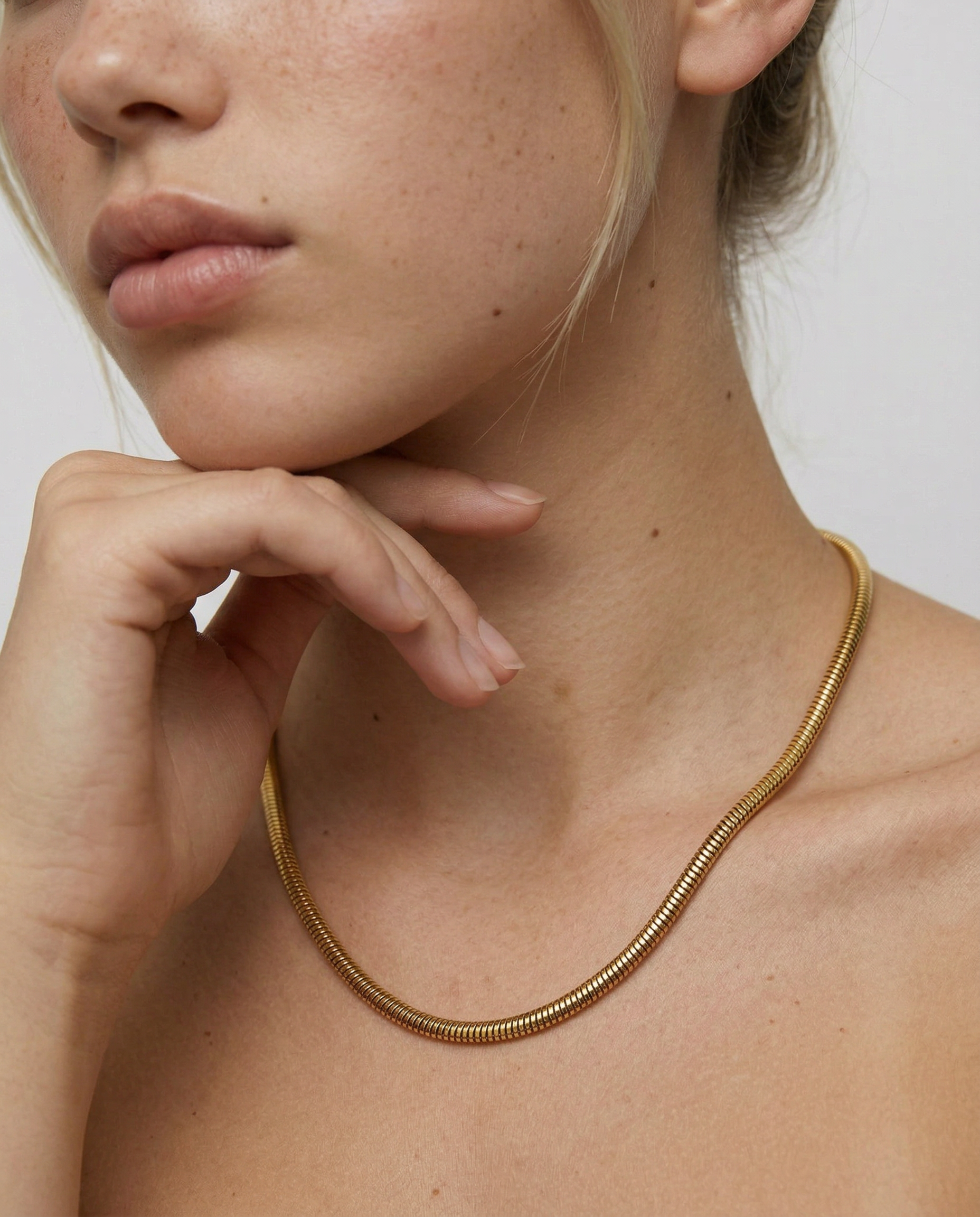 Close-up of a person wearing a gold necklace against a neutral background