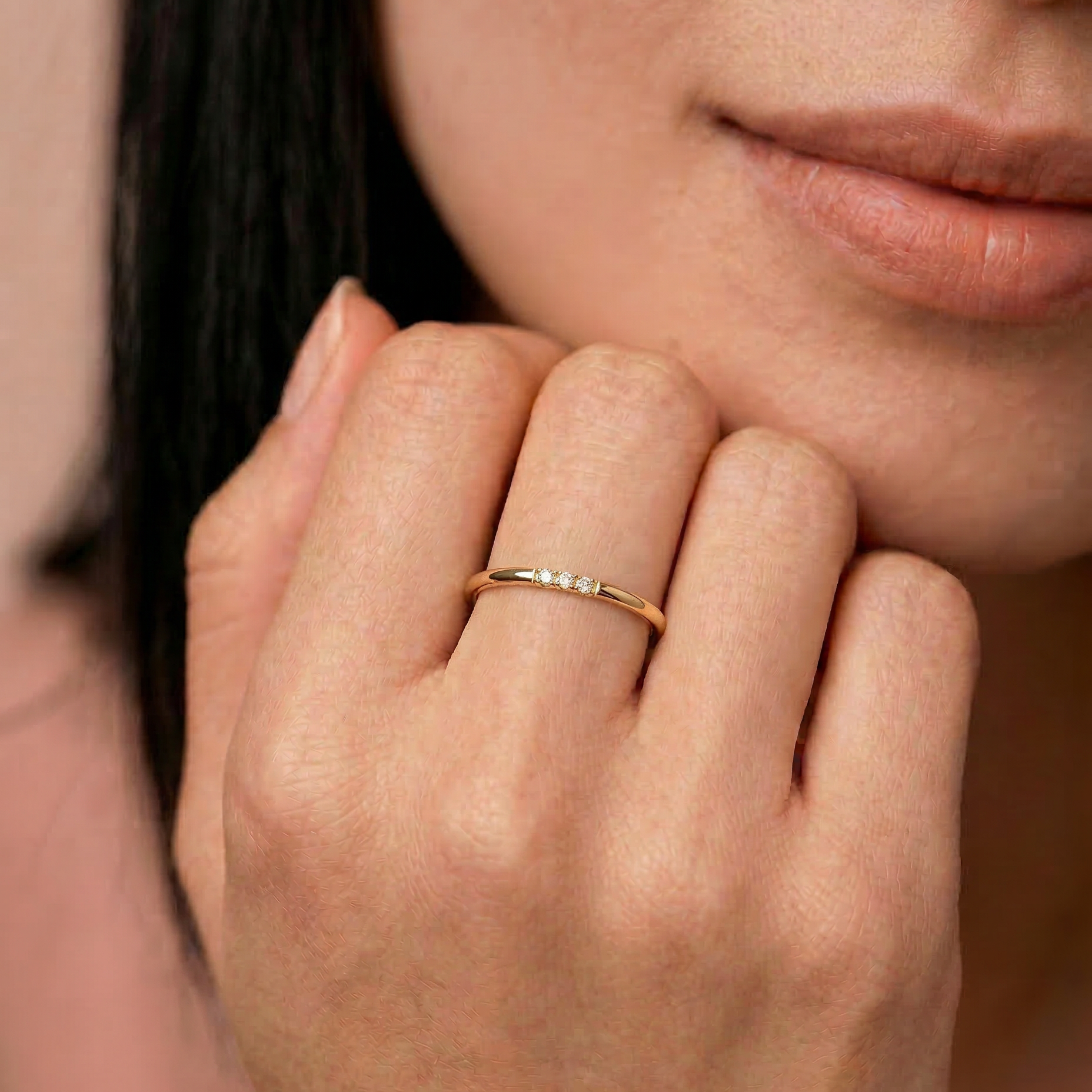 Close-up of a woman's hand wearing a gold ring with a soft focus on her face.
