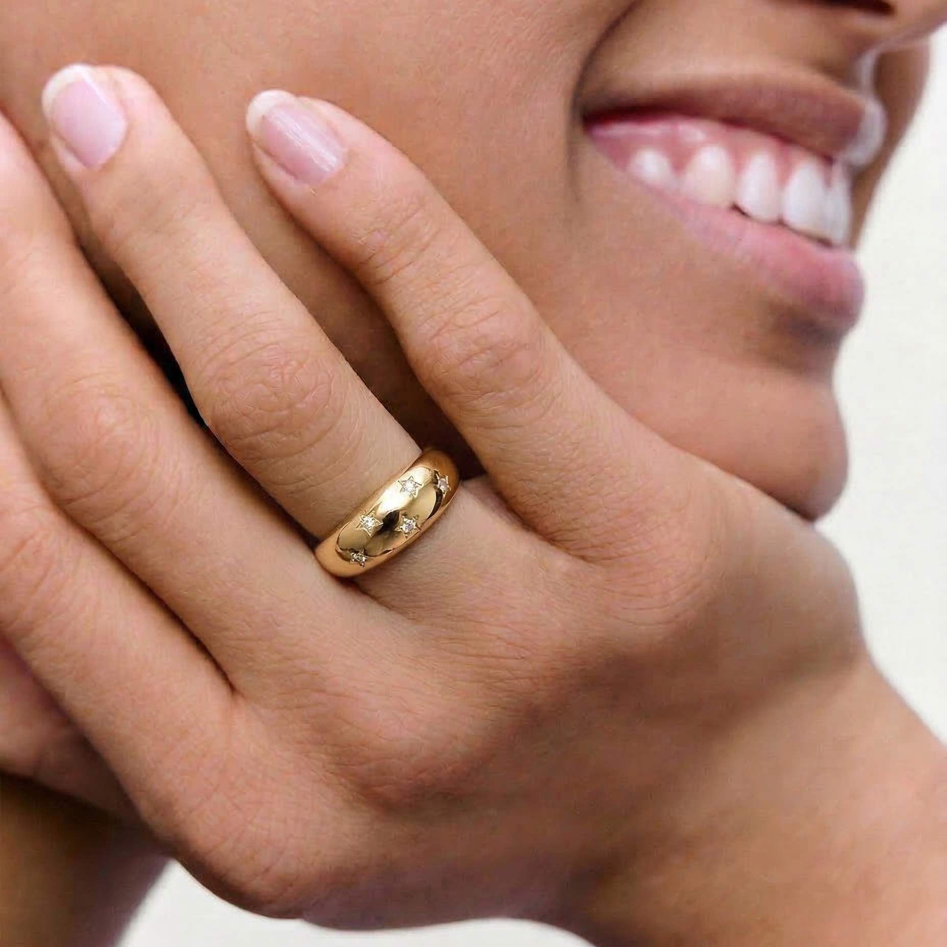 model wearing a gold-plated ring with a smooth, domed surface adorned with five star-shaped bezels containing crystals