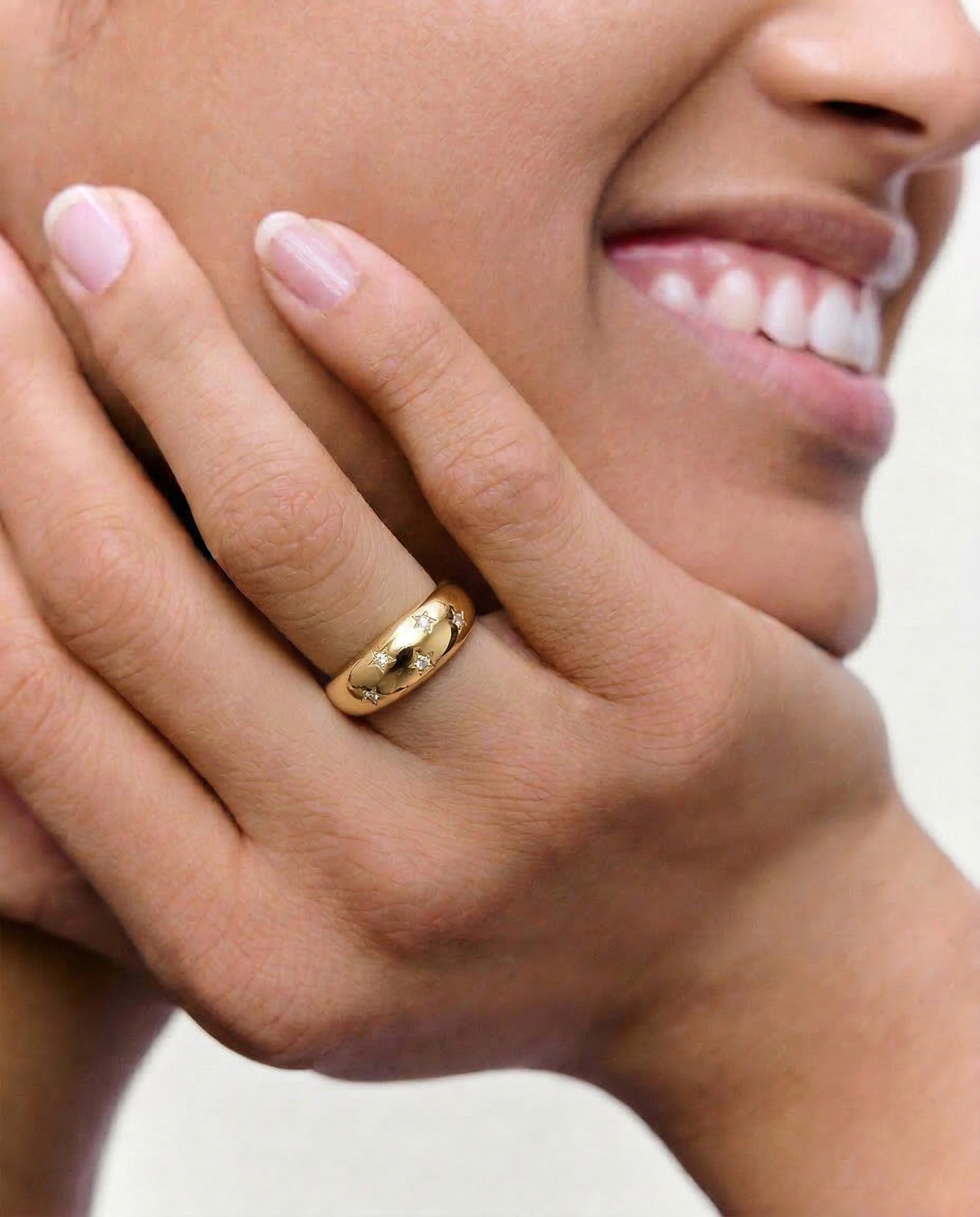 model wearing a gold-plated ring with a smooth, domed surface adorned with five star-shaped bezels containing crystals