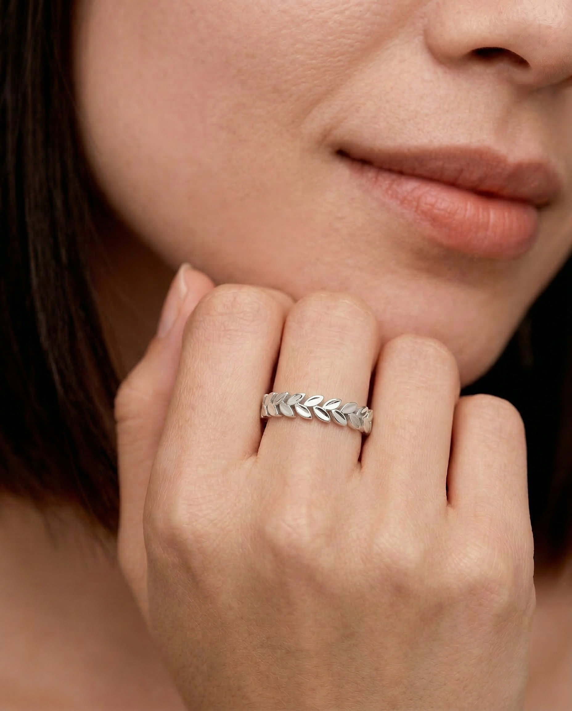 closeup shot of a model wearing a sterling silver laurel leaf band ring with a polished finish, featuring a series of leaves encircling the finger.