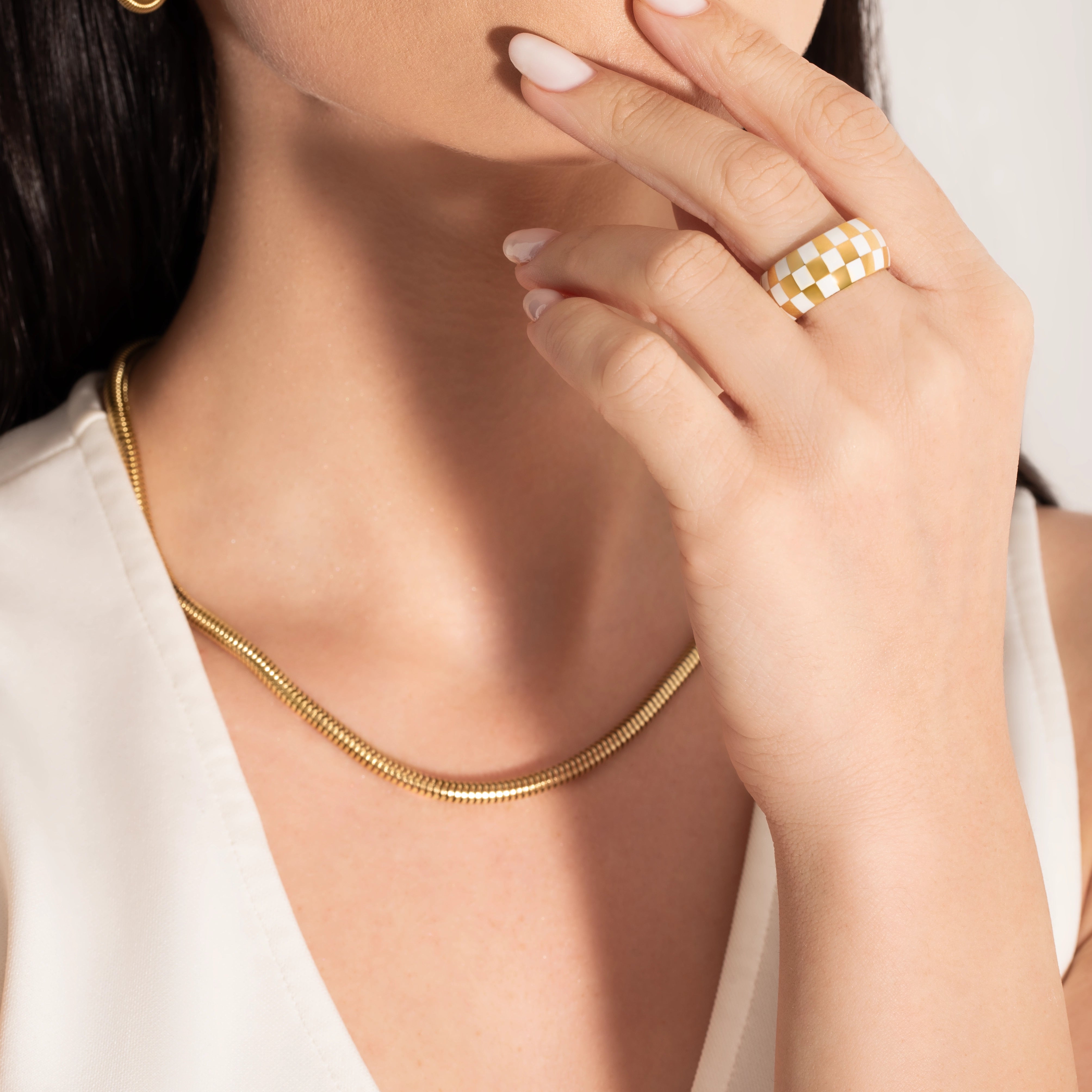 model wearing a big statement checkers board ring  and a snake chain necklace