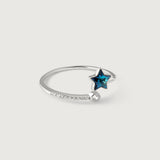 A sterling silver ring with a blue topaz star in the center, surrounded by smaller sparkling gemstones on the band, on a white background.