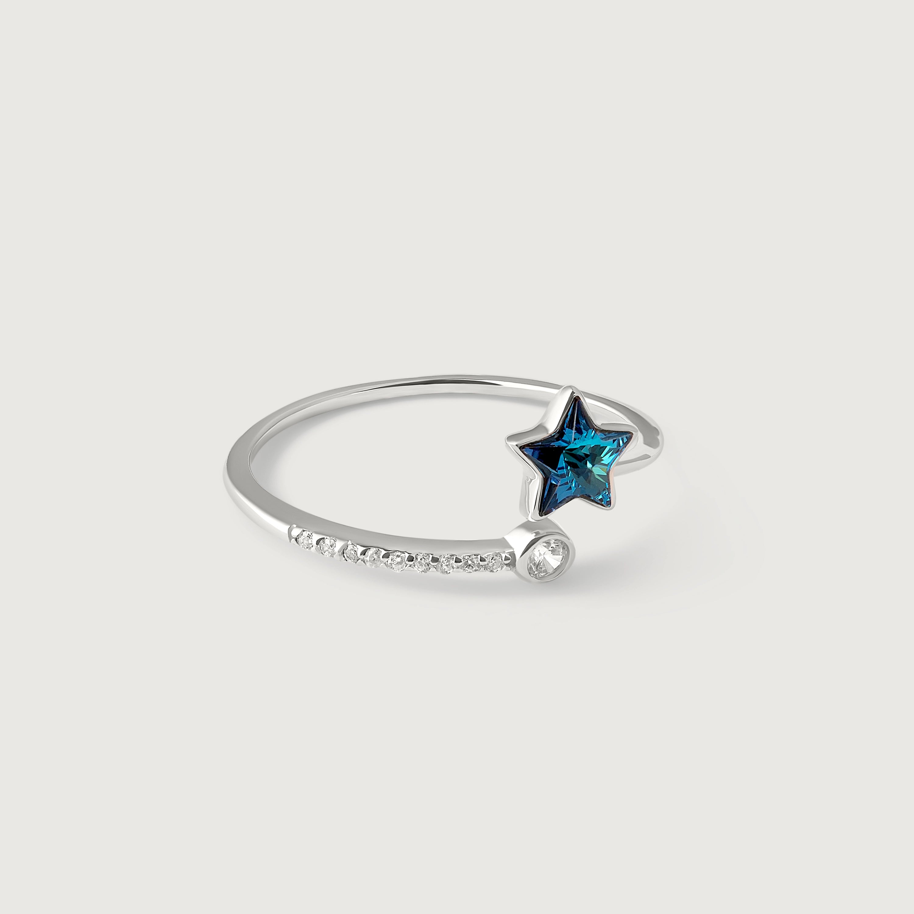 A sterling silver ring with a blue topaz star in the center, surrounded by smaller sparkling gemstones on the band, on a white background.