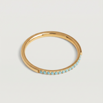 A minimalist gold band with a partial pavé of turquoise stones on the top half, displayed against a white background.