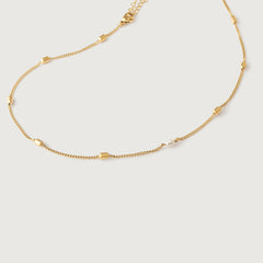 A gold-plated curb chain necklace with rectangular stations and a single pearl accent, displayed against a white background