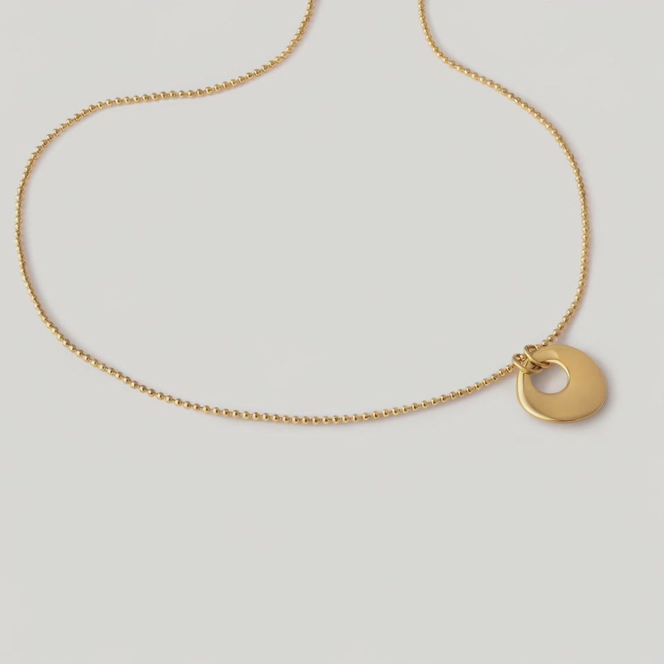 video of a gold-plated necklace with a circular charm