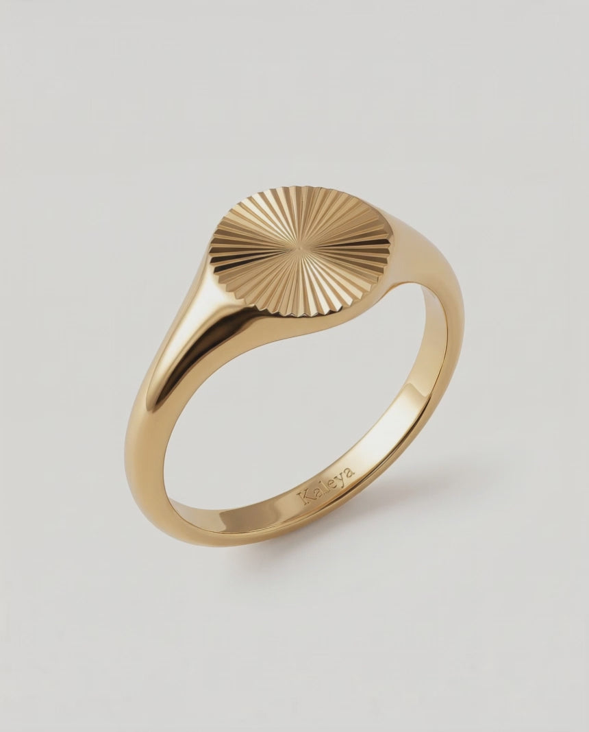 a video of a gold-plated signet ring with an oval face featuring a sunburst pattern