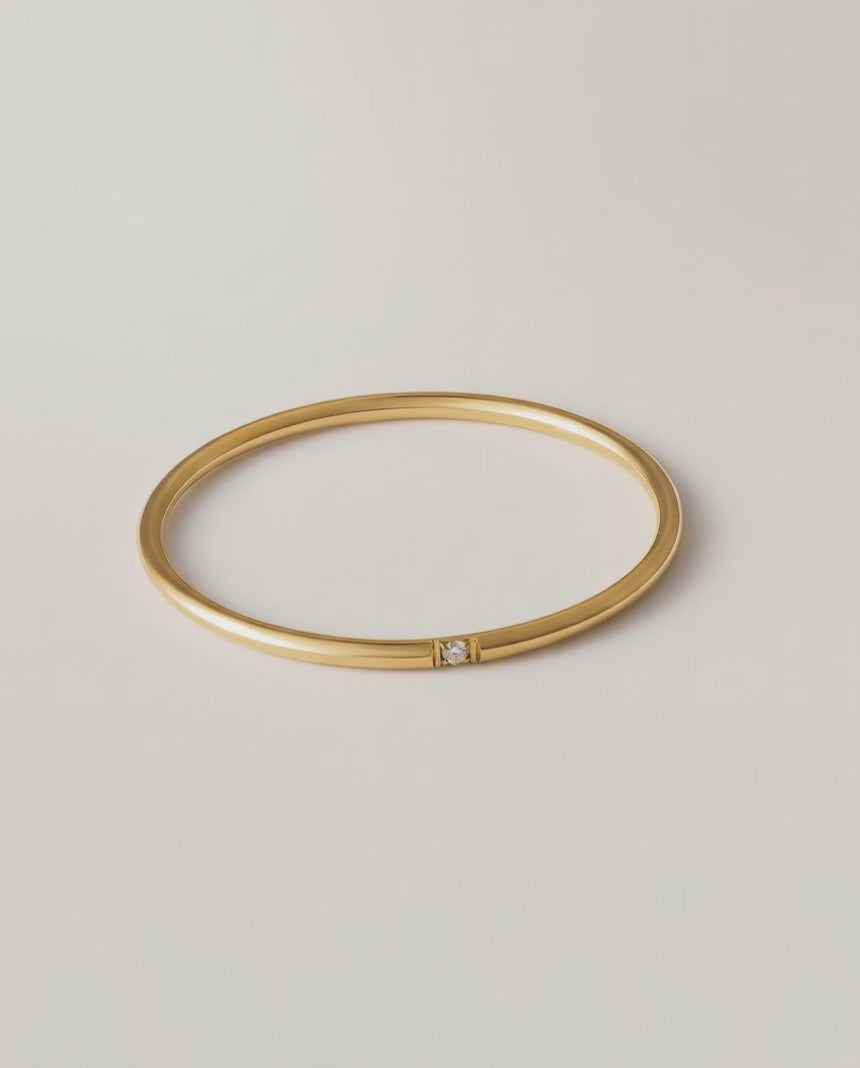360 rotating video of a gold-colored band ring with a single sparkling stone on a white background.