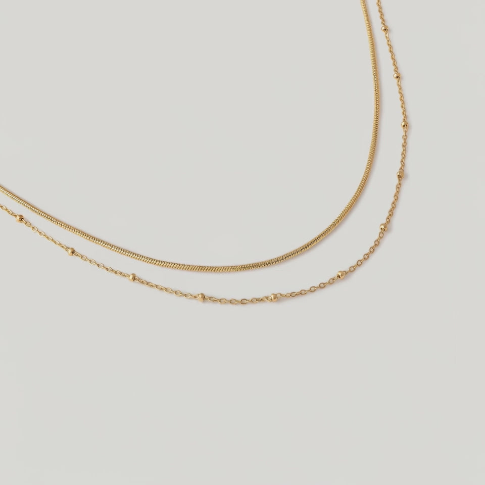 video of a layered choker necklace with one sleek snake chain and another with tiny spherical stations, both in 18k gold plating.