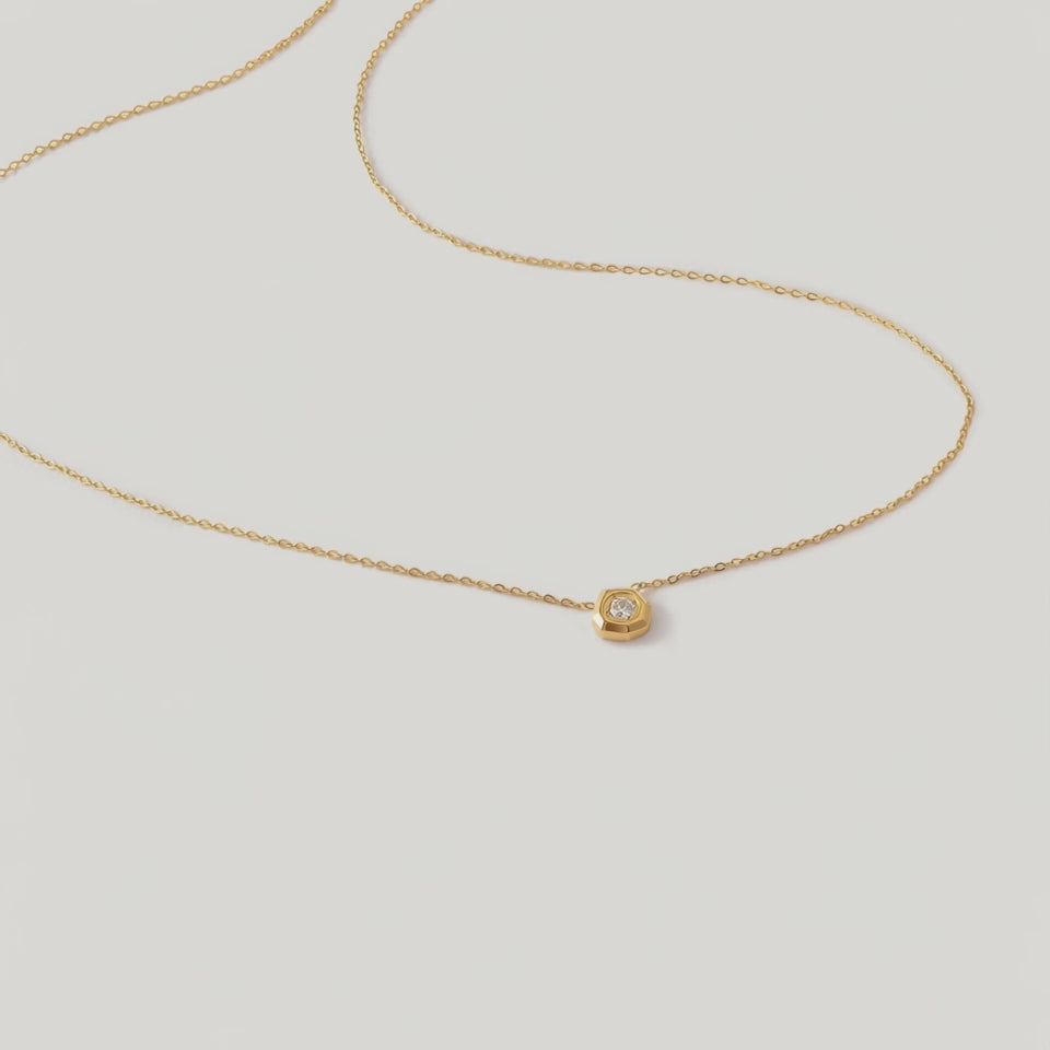 rotating video of a delicate gold-plated necklace with a hexagonal setting and a single crystal pendant.