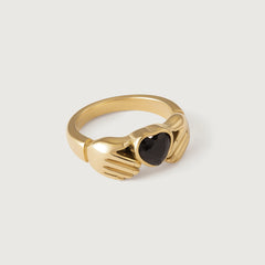 A gold-plated Claddagh ring with a heart-shaped black gemstone, featuring two hands holding a heart and a crown on top.