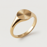 A gold-plated signet ring with an oval face featuring a sunburst pattern, displayed against a white background