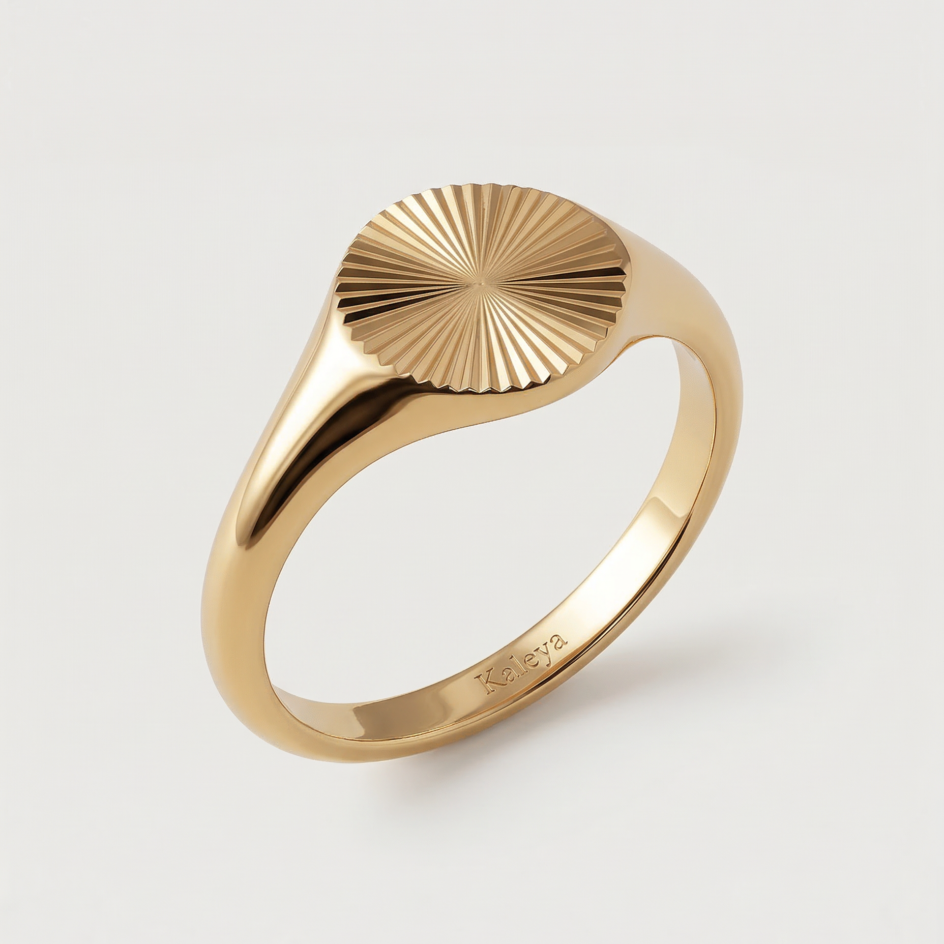 A gold-plated signet ring with an oval face featuring a sunburst pattern, displayed against a white background