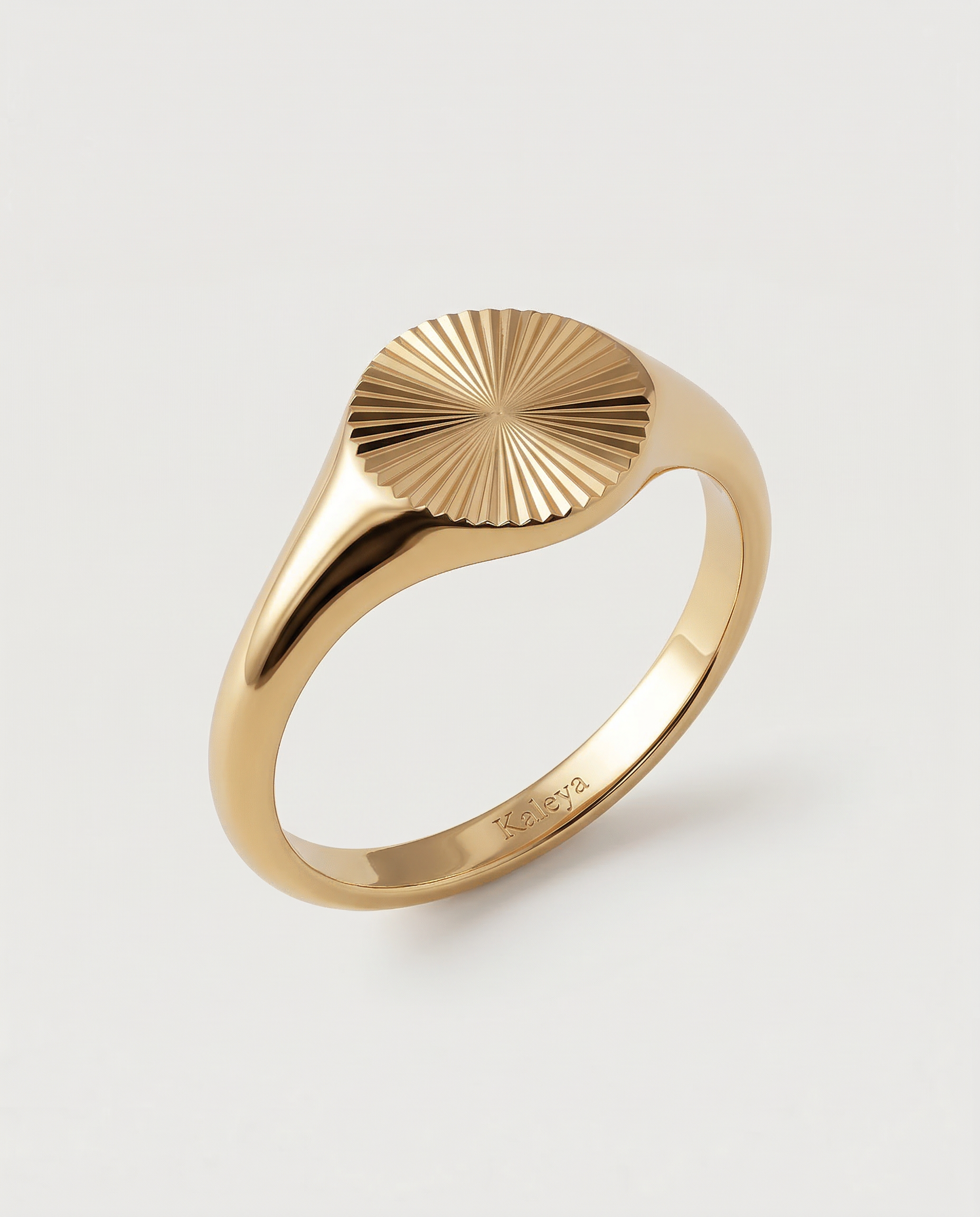 A gold-plated signet ring with an oval face featuring a sunburst pattern, displayed against a white background
