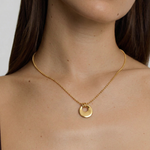 model wearing a gold-plated necklace with a circular charm