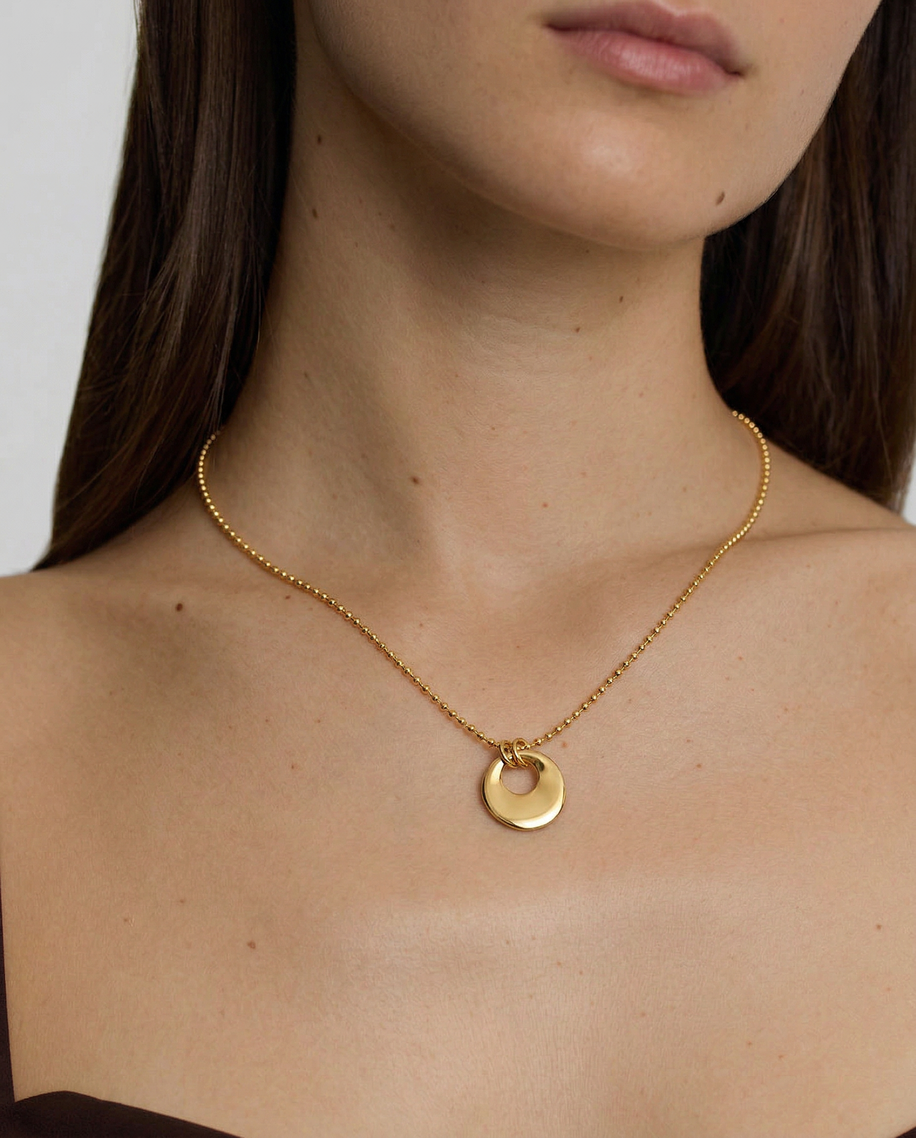 model wearing a gold-plated necklace with a circular charm