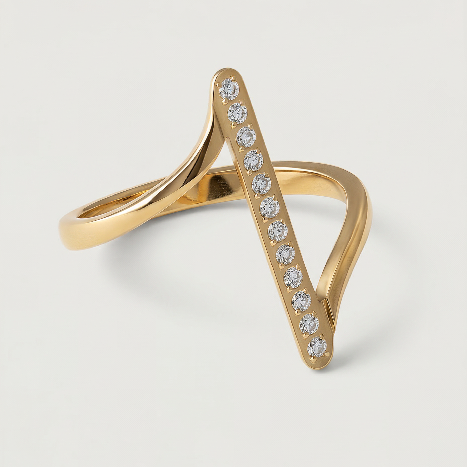 A contemporary gold-plated ring with an asymmetric design featuring a sleek bar adorned with a line of sparkling stones, presented against a white background.